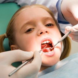 Photo of small girl looking at camera with open mouth while having teeth examined.