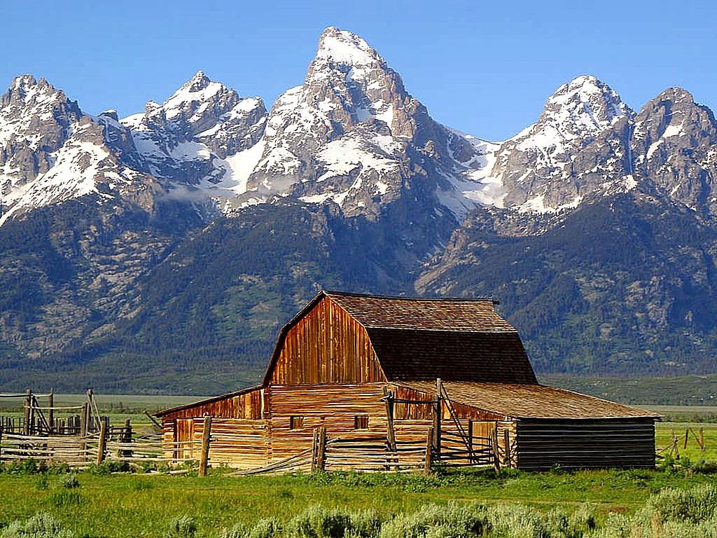 A weathered, old barn with a corral in front of the rugged, snow-capped Grand Teton mountains of Wyoming, USS.