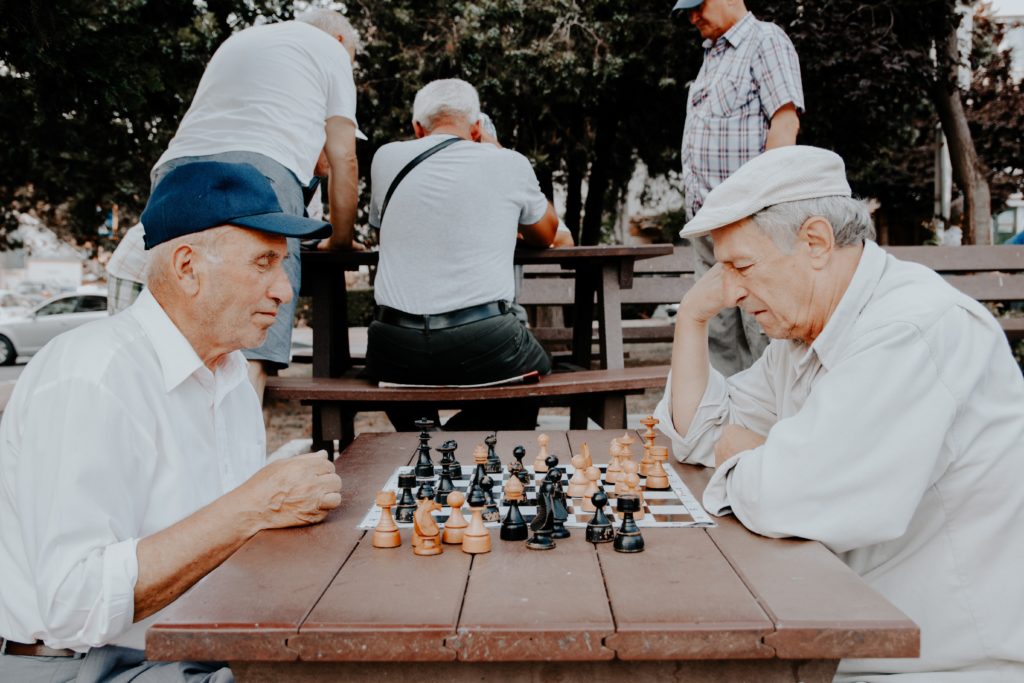 Two older men playing chess outside on a table in a park.