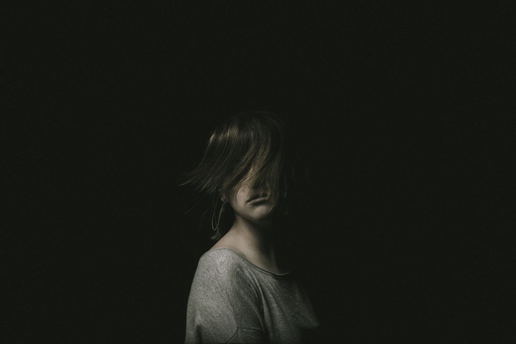 Picture of a young woman in a dark room, her eyes hidden from view by her hair