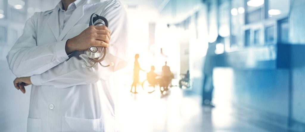 Picture of a doctor standing in a hospital hallway with arms crossed holding a stethoscope