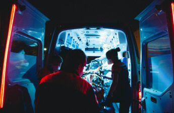 Three emergency medical technicians work at the back door of an ambulance at nigh