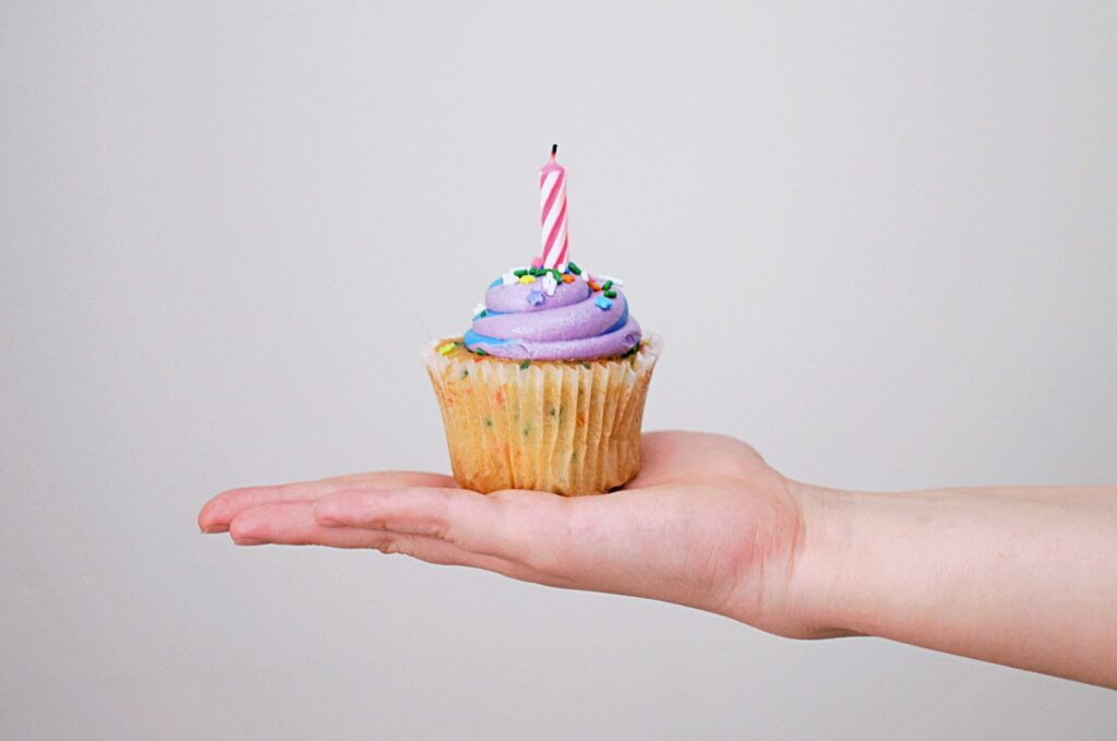 A hand holding a cupcake with a candle in it.