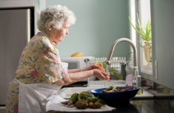 Elderly woman at sink washing and preparing food