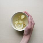 A photograph of a woman's hand cradling a cup of ginger tea.