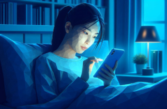 Young asian woman in bead at night reading from a smart phone bathed in the blue light from the phone's screen.