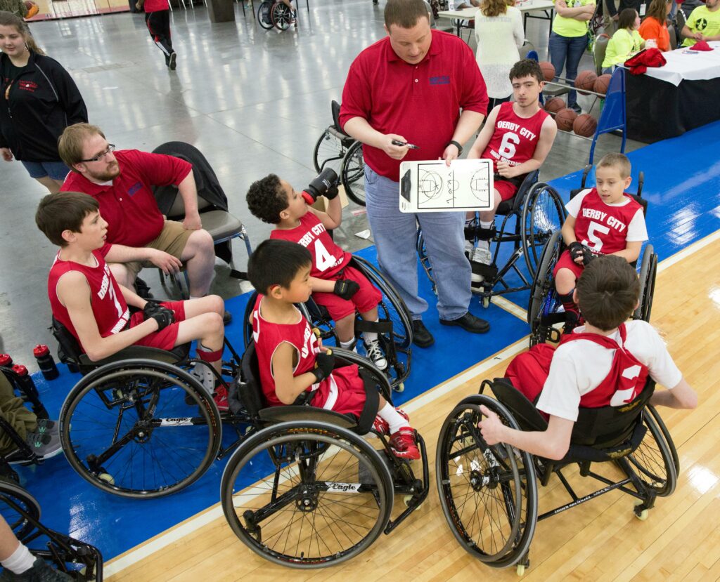 Picture of a grade school basketball team made up of disabled athletes huddling with their coach looking play diagrams on a clipboard.