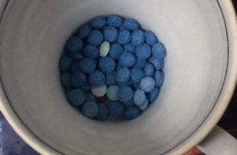 A shot into a cup filled containing blue fentanyl-laced pills.